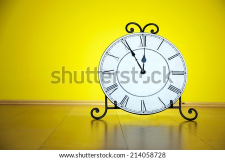 Old antique wall clock isolated on wooden floor and yellow wall background, five minutes to twelve o'clock