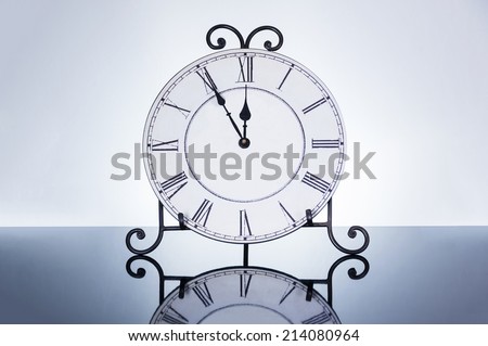 Old antique wall clock isolated on reflective floor, five minutes to twelve o'clock