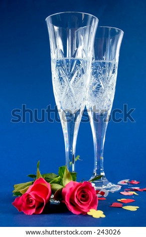 Focus on first glass. confetti and roses at base of champagne flutes