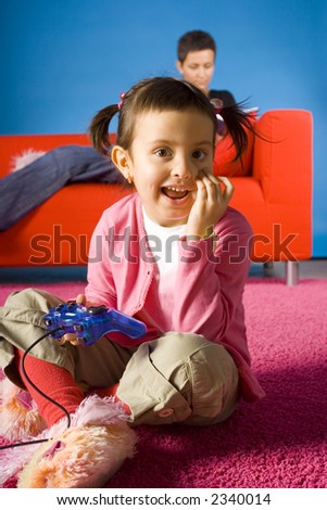 happy girl sitting on the carpet and playing video game and  her busy (with book) mother on the sofa