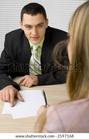 Man and woman at the office desk. Man's pointing paper and talking.