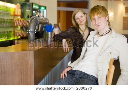 Man and woman are sitting at the bar and looking at the camera. Short depth of focus on man\'s face.