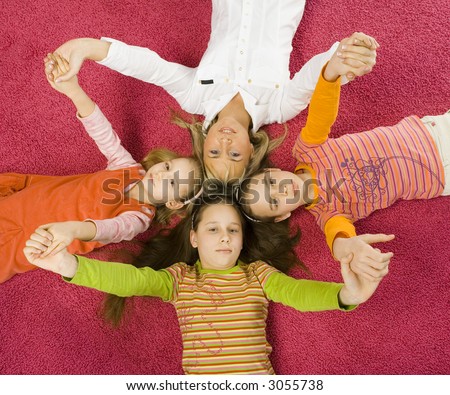 3 girls and their mother are lying on pink carpet and looking at camera. They\'re touching by their heads. They\'re holding their hands up.