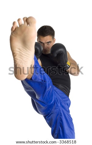 Young man in black boxing gloves doing flying side kick to the camera. Isolated on white in studio, looking at camera. Closeup on foot
