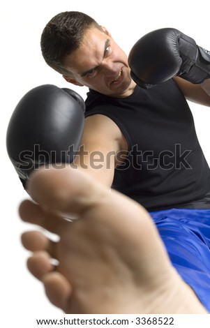 Angry young man in black boxing gloves doing flying side kick to the camera. Isolated on white in studio, looking at camera.