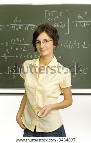 Teenage girl standing in classroom, in front of blackboard. Smiling and holding chalk. Looking at camera