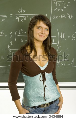 Teenage girl standing in classroom, in front of blackboard. Smiling, looking at camera
