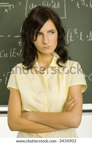 Teenage girl standing in classroom, in front of blackboard with crossed arms. front view