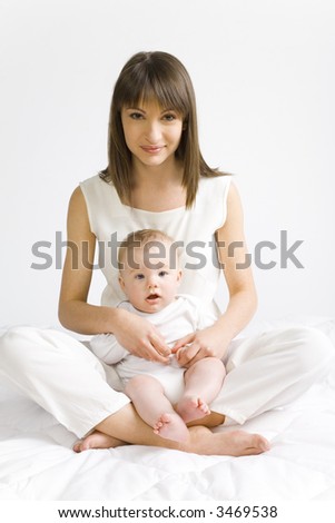 Young mother with baby boy. Sitting on white cloth. Looking at camera. Whole body, front view