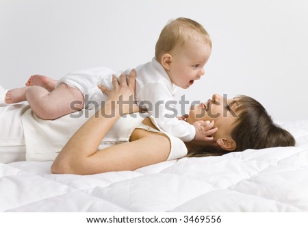 Young mother with baby boy. Lying on bed and hugging. Face to face, side view