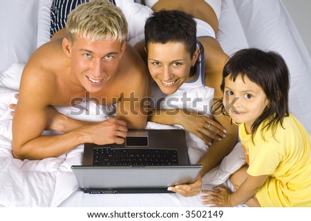 Happy family lying in bed in front of laptop. Smiling and looking at camera