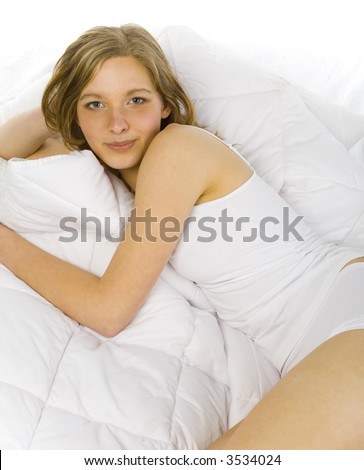 Young, beautiful woman lying in bed on white duvet. Looking at camera