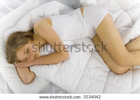 Young, sad beautiful woman lying in bed on white duvet
