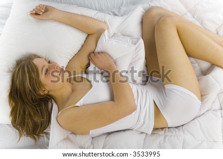 Young, smiling beautiful woman lying in bed on white duvet