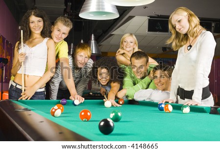 Large group of teenagers standing at pool table. Smiling and looking at camera. One person is playing billard