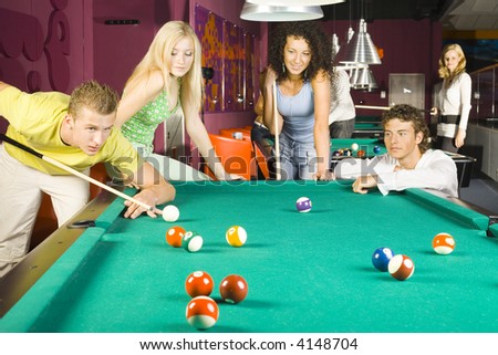 Large group of teenagers standing at pool tables. Smiling and playing billard. One person is very concentrated