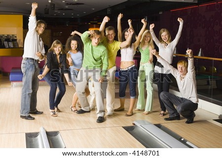 Large group of teenagers standing and cheering in bowling alley. One person crouching. Some of them are looking at camera
