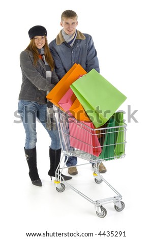 Young couple with full trolley. Smiling and looking at camera. Isolated on white in studio. Whole body