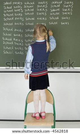 Little girl standing on chair in front of blackboard. Writing on it. Rear view, whole body