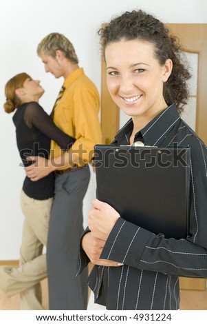 Three people standing in flat. One couple is hugging, other woman is standing alone and looking at camera. Everyone smiling
