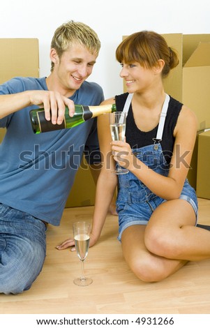 Young couple sitting on the floor in flat. They\'re looking happy. Celebrating removal with champagne