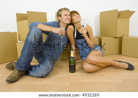 Young couple sitting on the floor in flat. They\'re looking happy. Celebrating removal with champagne. Whole body