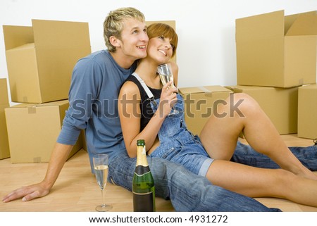 Young couple sitting on the floor in flat. They're looking happy. Celebrating removal with champagne