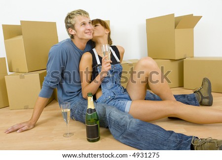 Young couple sitting on the floor in flat. They're looking happy. Celebrating removal with champagne. Woman is kissing man