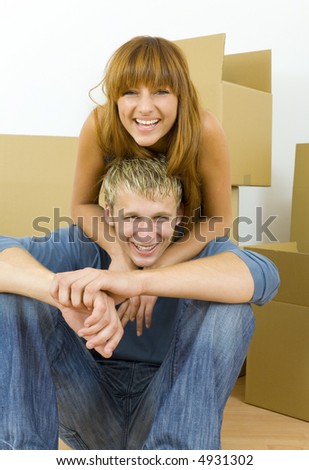 Young couple sitting on the floor in flat. They're looking happy. Woman is hugging man. They're looking at camera. Front view