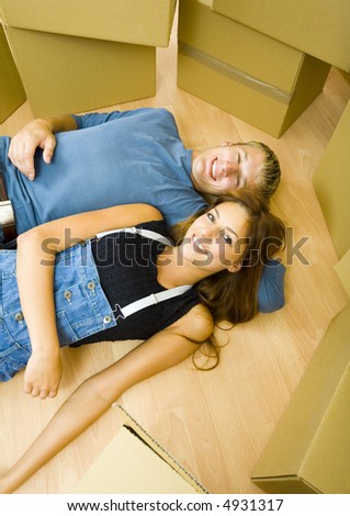 Young, happy couple lying on the floor in flat and resting.They\'re looking at camera. Front view