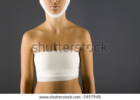 Young, unhappy woman with bandage on head and breast. Front view, gray background