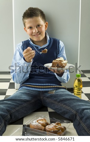 Smiling boy sitting on the floor with cake on dessert plate. Front view. Looking at camera.