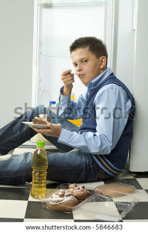 Boy sitting on the floor and eating cake. Side view. Looking at camera.