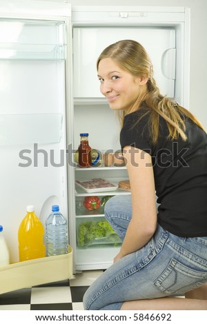 Young woman kneeling in front of the frige. She\'s smiling and looking at camera.