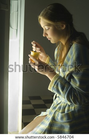 Young woman in front of the fridge eating yogurt. Side view.
