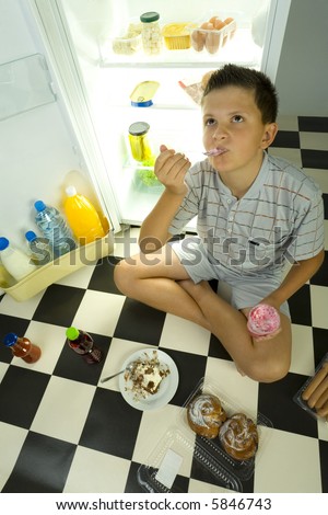 Young boy sitting by the fridge and eating ice cream. High angle view