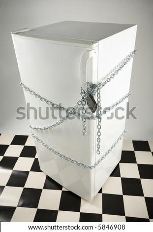 Closed fridge enwinded by chain and lock. Grey background. High angle view.