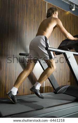 Young man without shirt running on track in gym. Whole body, rear view