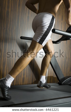 Young man with running on track in gym. We don\'t see his face. Side view