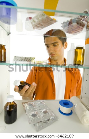 Young man looking at bottle of  cough syrup, He\'s standing in front of medicine chest.