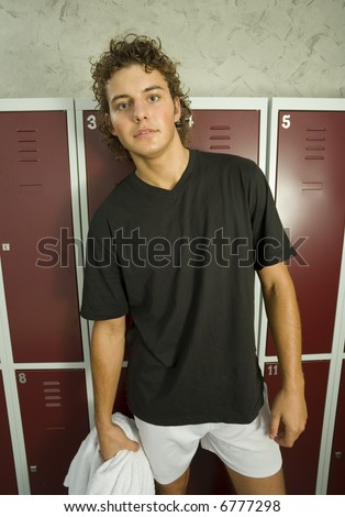 Young, tired man standing in locker room in front of lockers. Holding towel in hand. Front view. Looking at camera