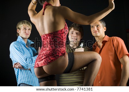 Three men standing in front of dancing woman in dark room. They are smiling but one looking confused