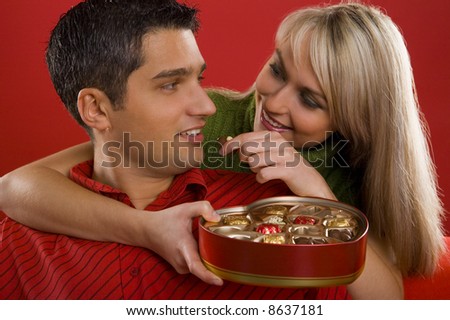 Young enamoured couple. Woman is feeding man by chocolate and smiling. Front view