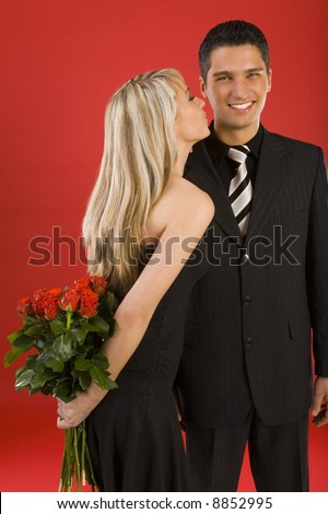 Young, happy couple. Woman is holding bouquet of roses and kissing man. The man is smiling and looking at camera