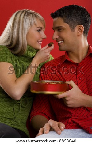 Young enamoured couple. Woman is feeding man by chocolate and smiling. Front view
