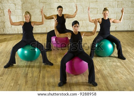 A group of women making exercise sitting on big balls with upraised hands. They\'re looking at camera. Front view.