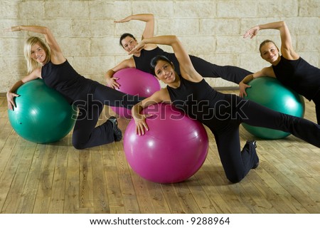 A group of women making exercise leaning on big balls. They\'re smiling and looking at camera. Front view.
