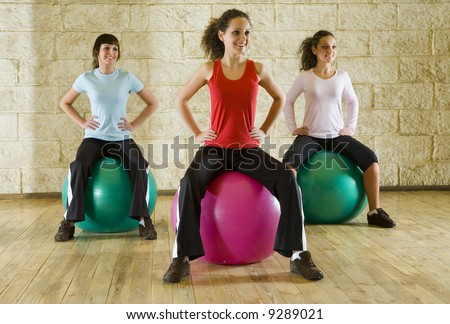 A group of women making exercise sitting on big balls and holding hands on hips. Front view.