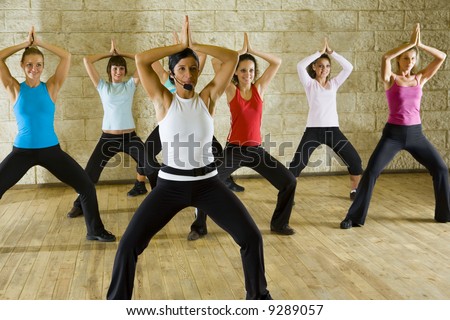 A group of women exercising with fitness instructor in the gym. Focus on the woman in white shirt. Front view.