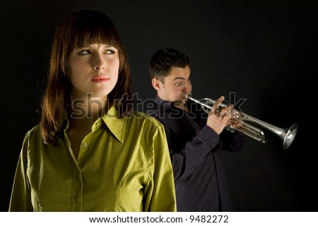 Trumpet man standing behind the woman. The woman looks thoughtful. Front view.